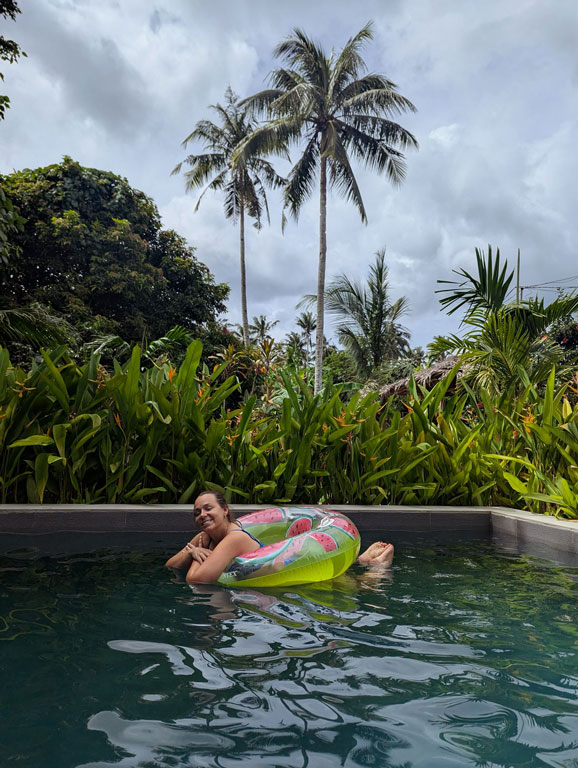 Person floating in a pool with palm trees and tropical garden in Palawan